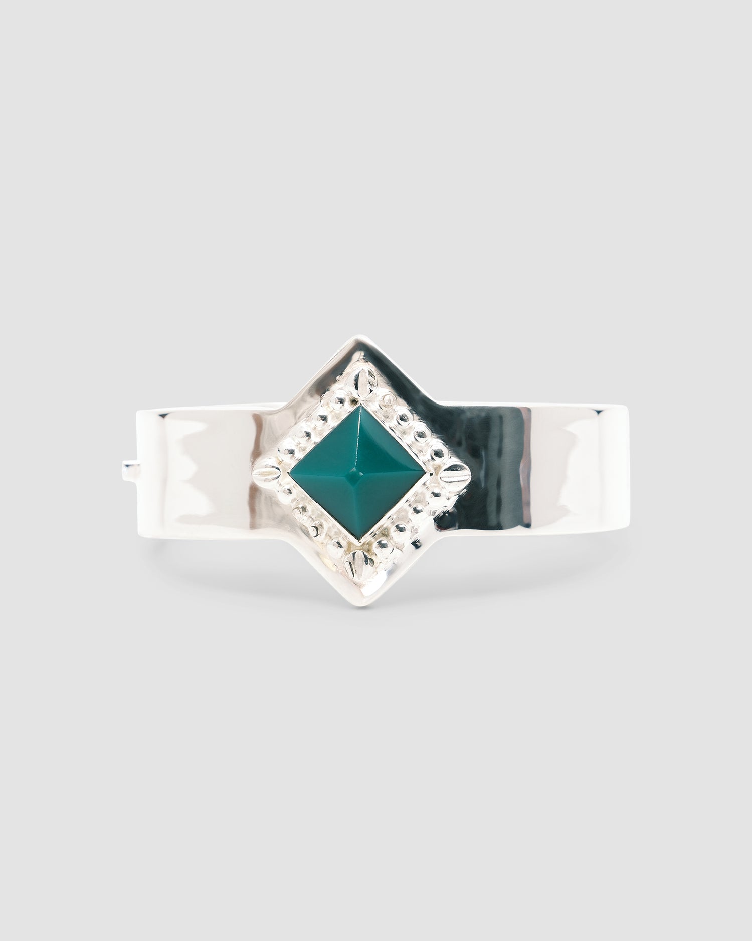 a silver cuff bracelet with a green sqaure stone set into it and beading around the exterior