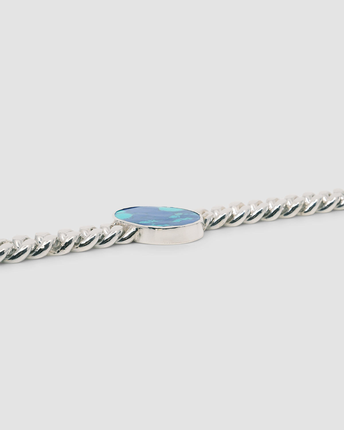 sterling silver cuban link bracelet sits on a grey background with a glimpse of a blue green inlaid stone