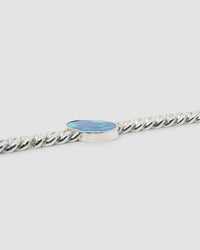 sterling silver cuban link bracelet sits on a grey background with a glimpse of a blue green inlaid stone