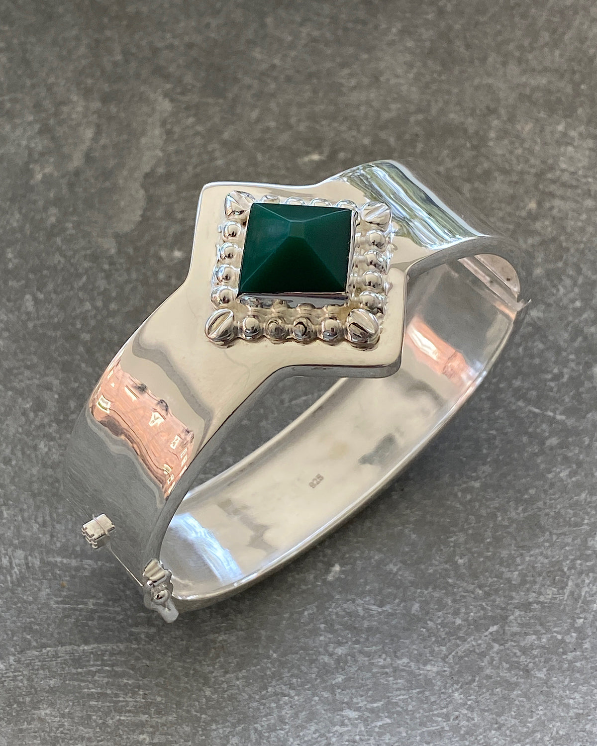 a silver cuff bracelet with a green sqaure stone set into it and beading around the exterior