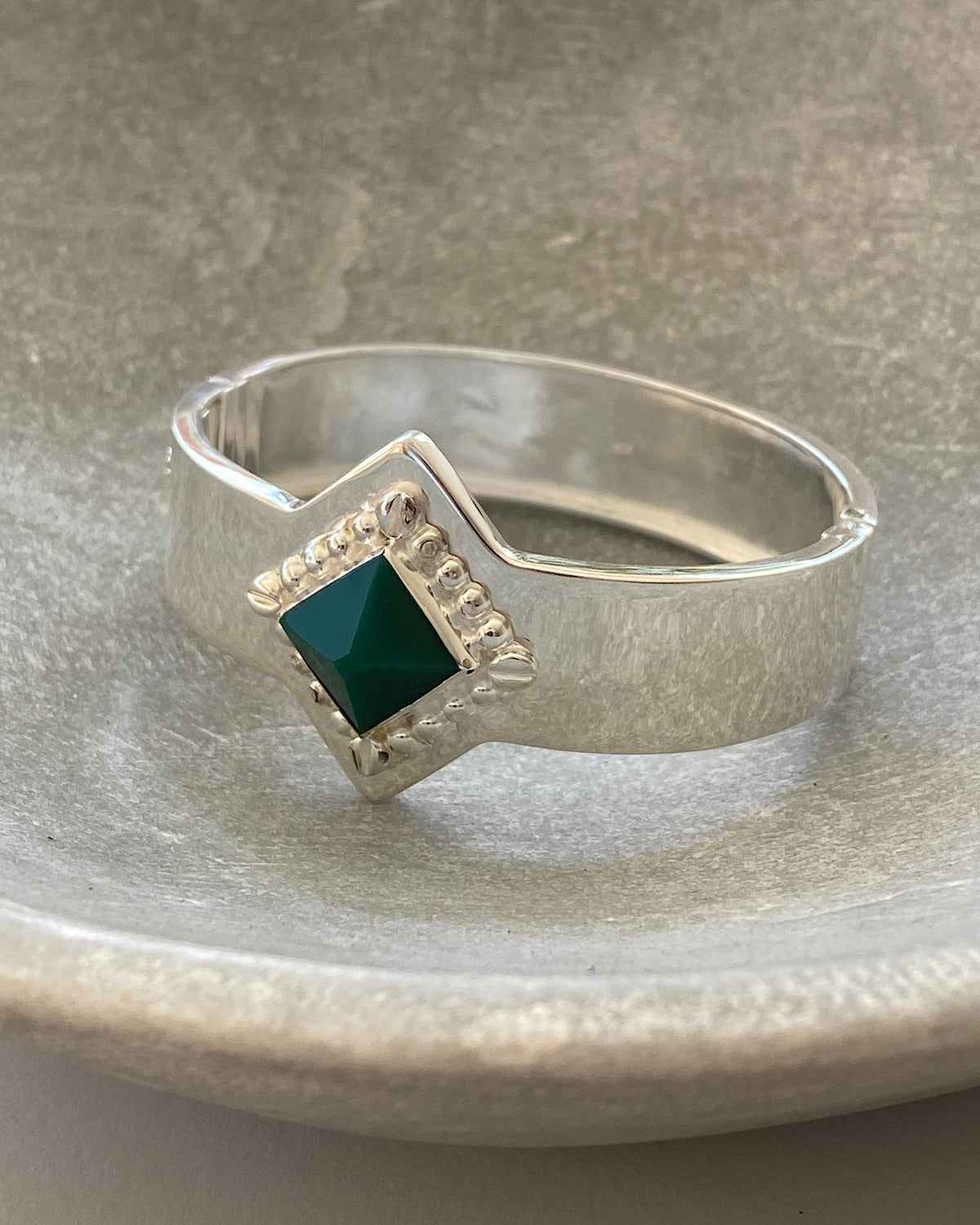 a silver cuff bracelet with a green sqaure stone set into it and beading around the exterior