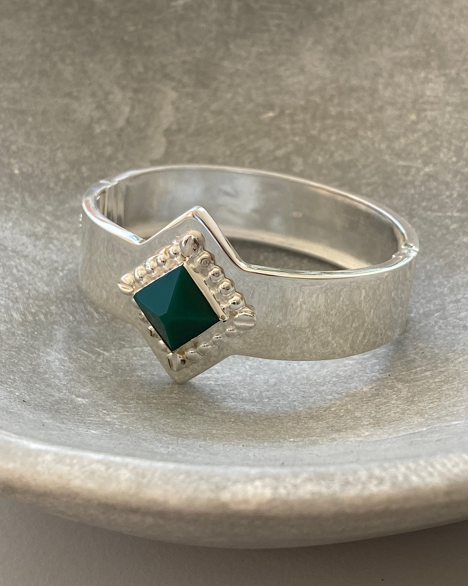 a silver cuff bracelet with a green sqaure stone set into it and beading around the exterior