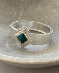 a silver cuff bracelet with a green sqaure stone set into it and beading around the exterior