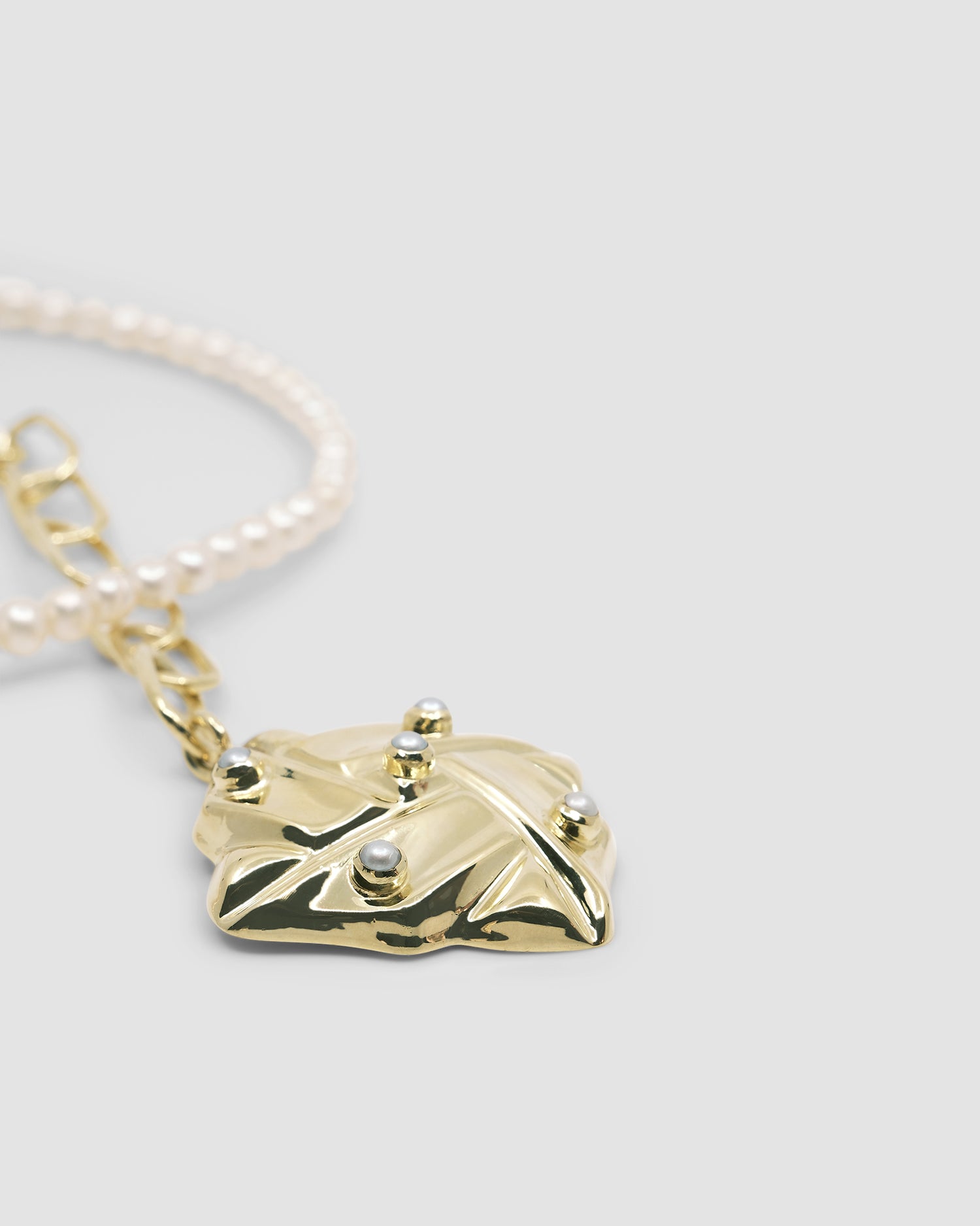 a vintage square gold woven pendant with pearls sits on a gold and pearl wrap style necklace