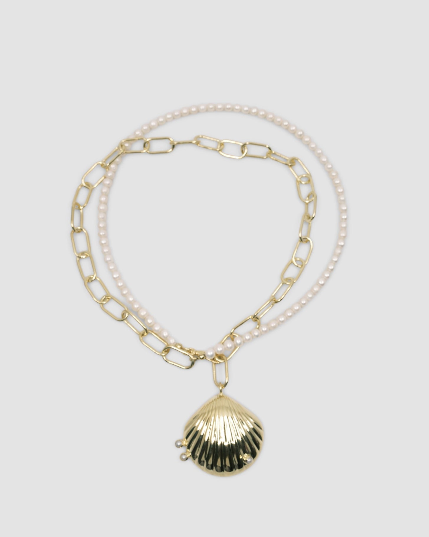 A gold shell pendant with pearls sit on a pearl & chain wrap style necklace