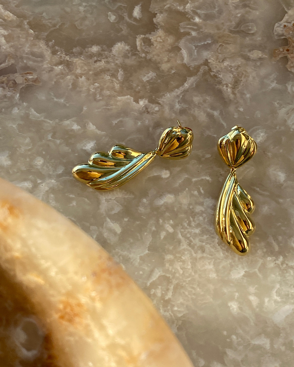 Gold sculptural drop earrings against a grey background