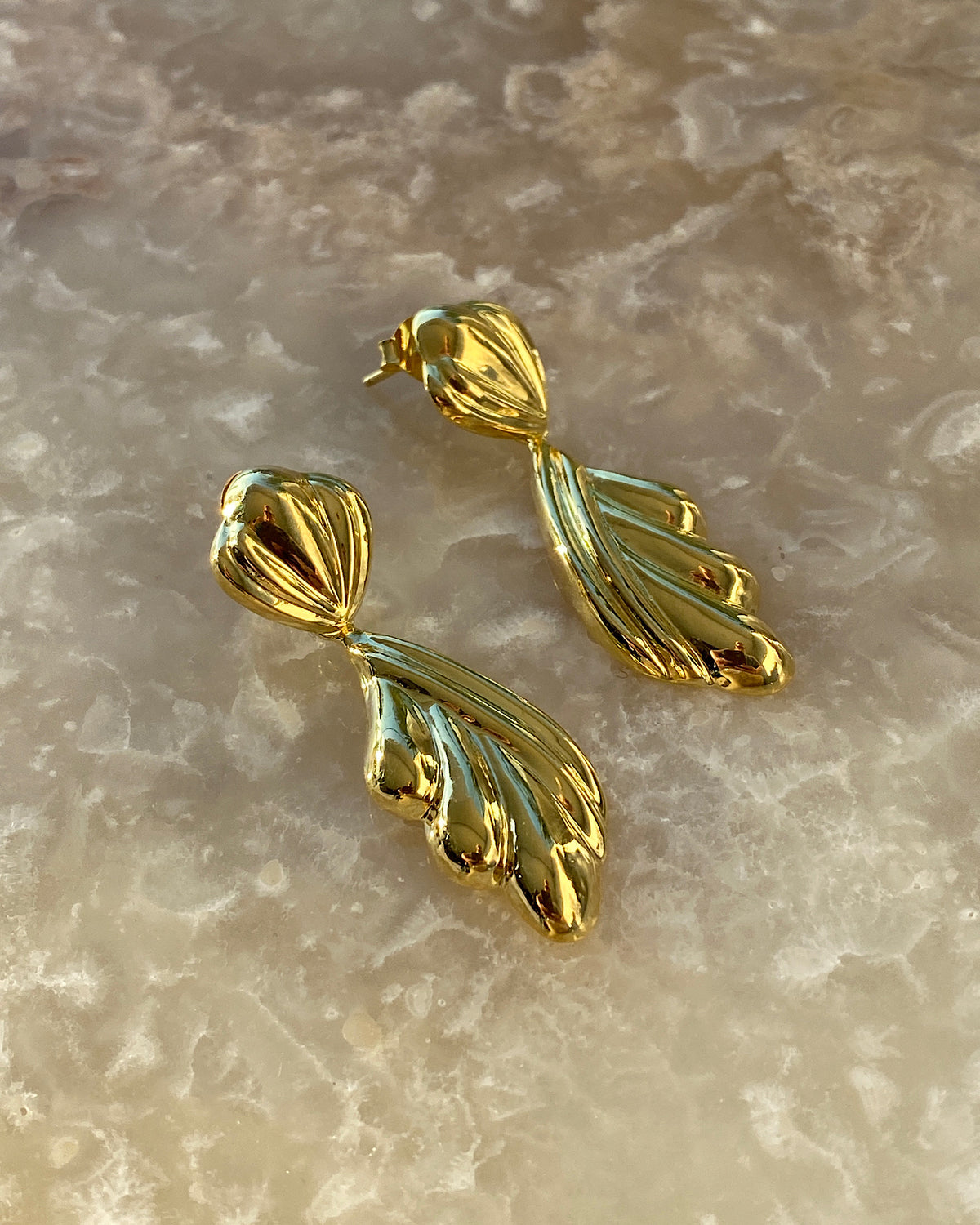 Gold sculptural drop earrings against a stone background