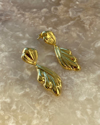 Gold sculptural drop earrings against a stone background