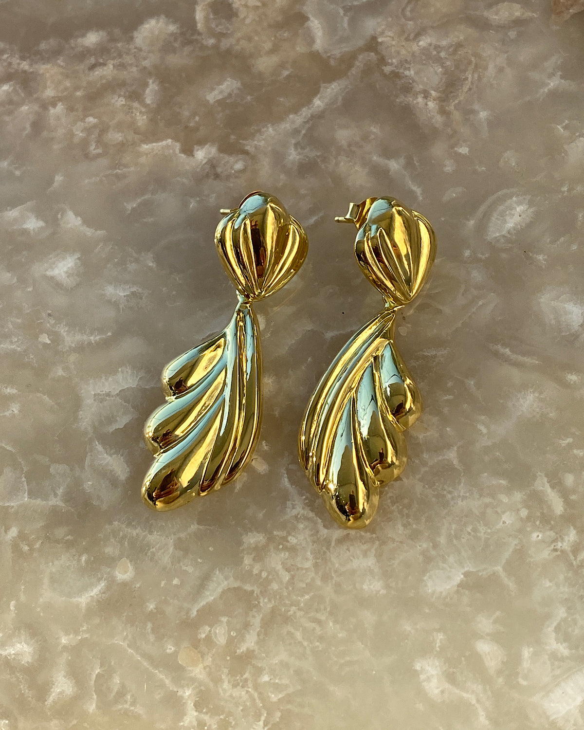Gold sculptural drop earrings against a stone background