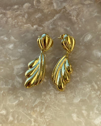 Gold sculptural drop earrings against a stone background