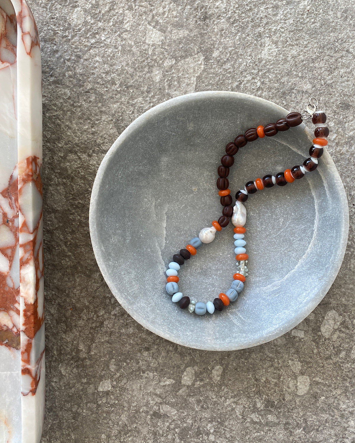 Earth toned assorted beaded glass and pearl necklace sits in a bowl