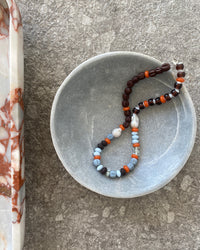 Earth toned assorted beaded glass and pearl necklace sits in a bowl
