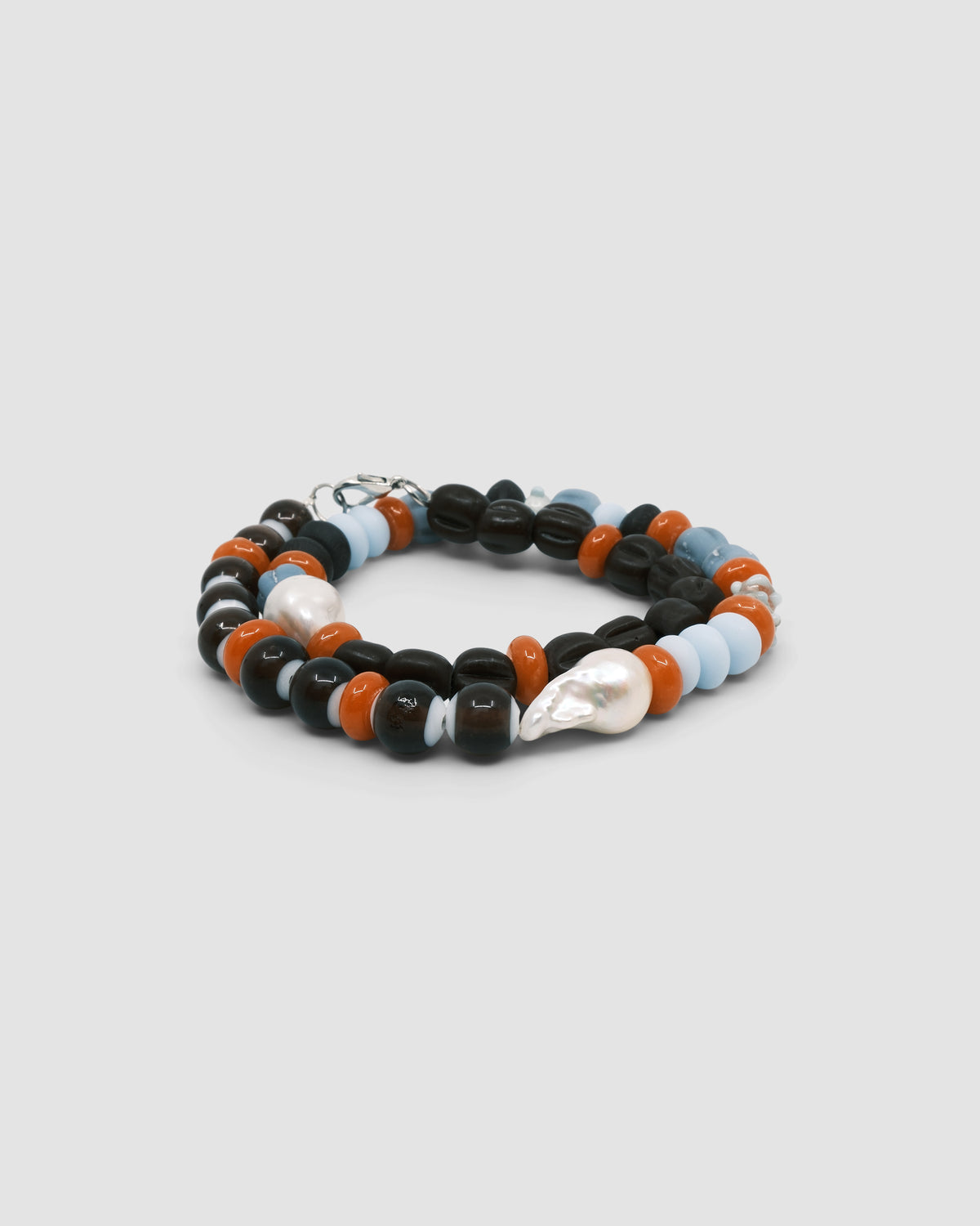 Earth toned assorted beaded glass and pearl necklace on a grey background