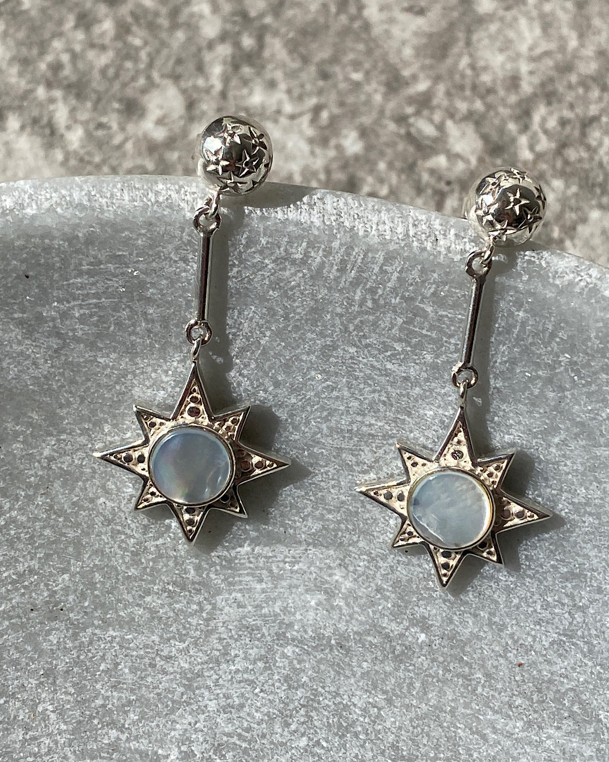 Silver star drop earrings with a shell inlaid centre sit in a stone bowl