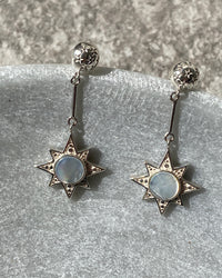 Silver star drop earrings with a shell inlaid centre sit in a stone bowl