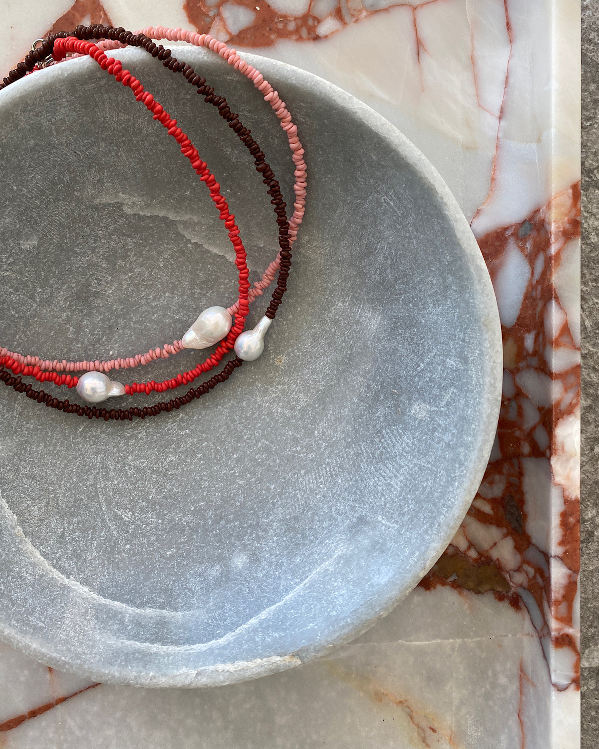 a single baroque pearl floats on a red bead necklace
