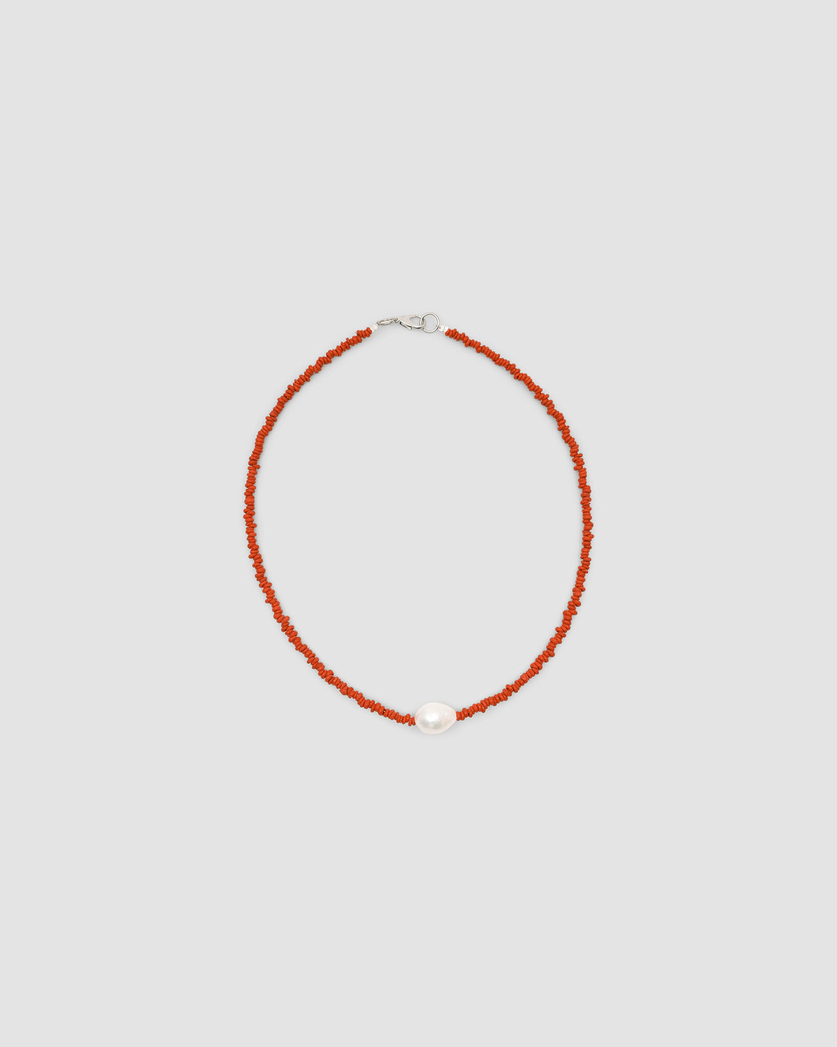 a single baroque pearl floats on a red bead necklace