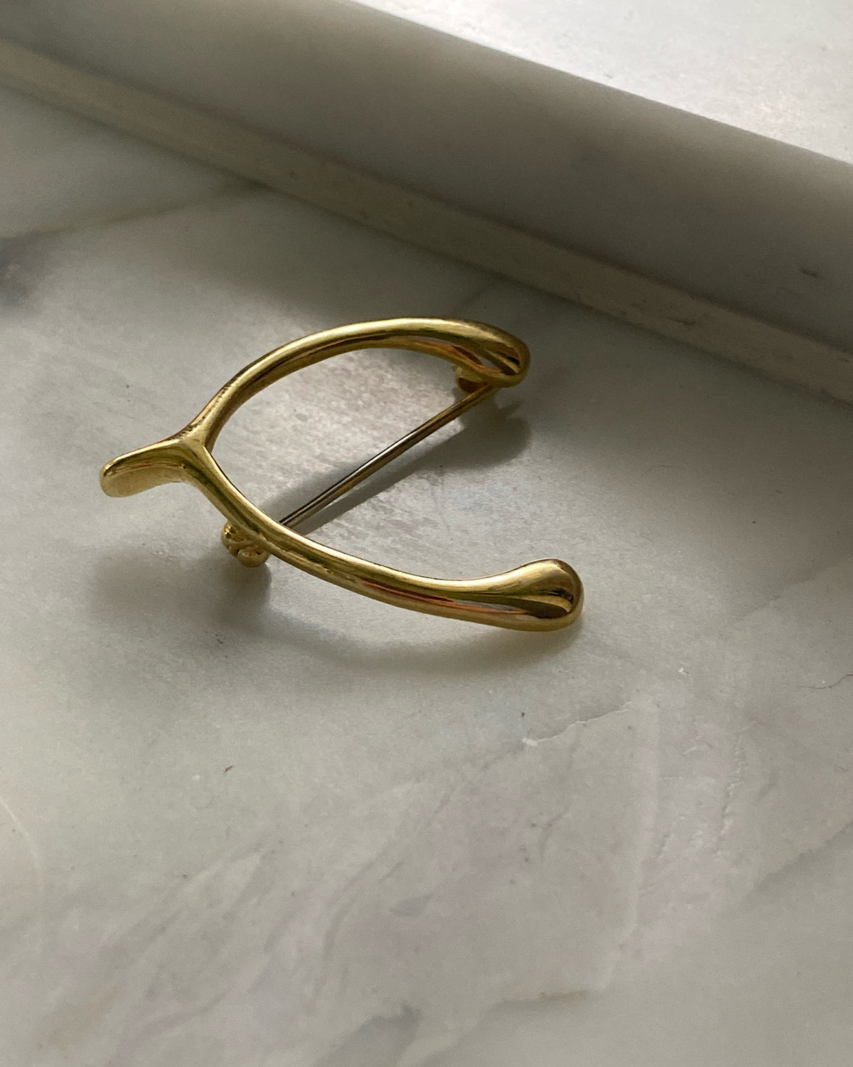a gold wishbone brooch sits on marble