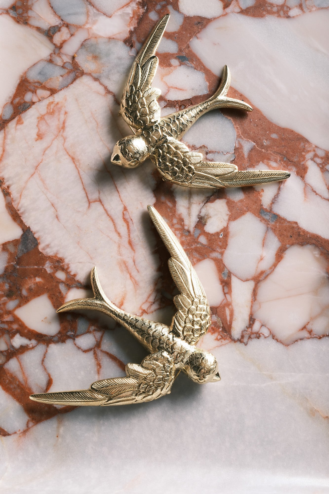 two large brass swallow brooches sit on marble