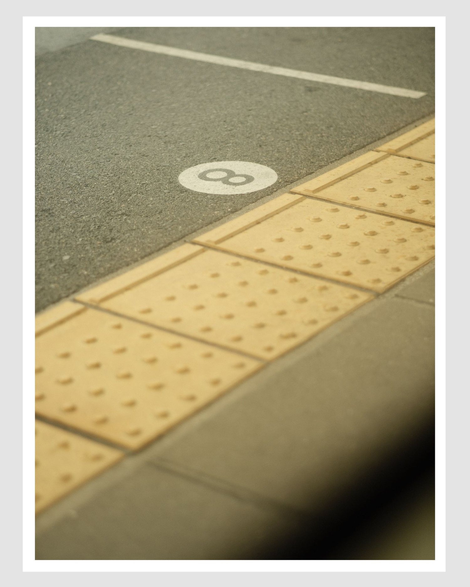Close-up of a tactile paving strip with a raised circle and dot on a road surface.