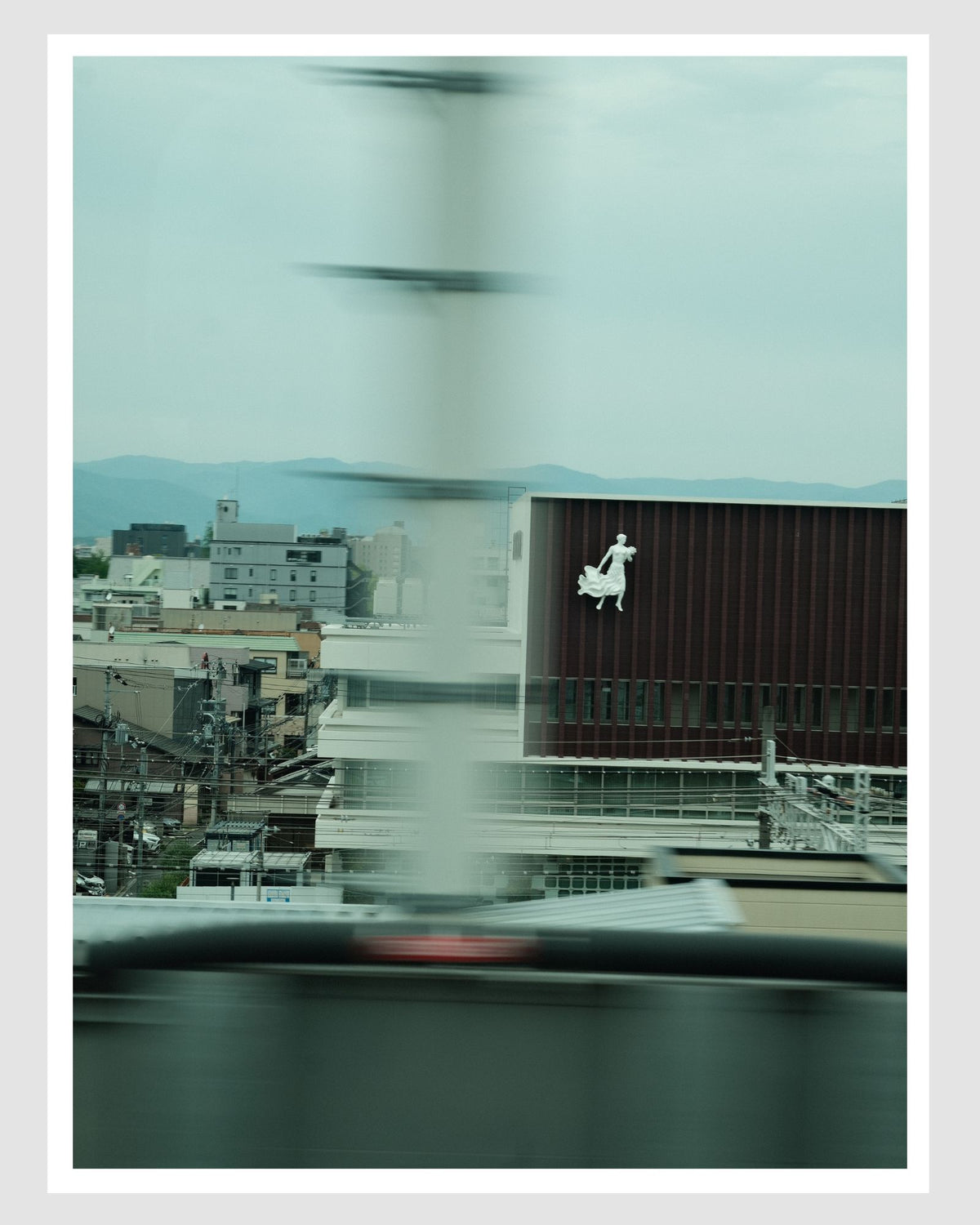 Cityscape view from a vehicle window with blurred motion, featuring a building with a logo.