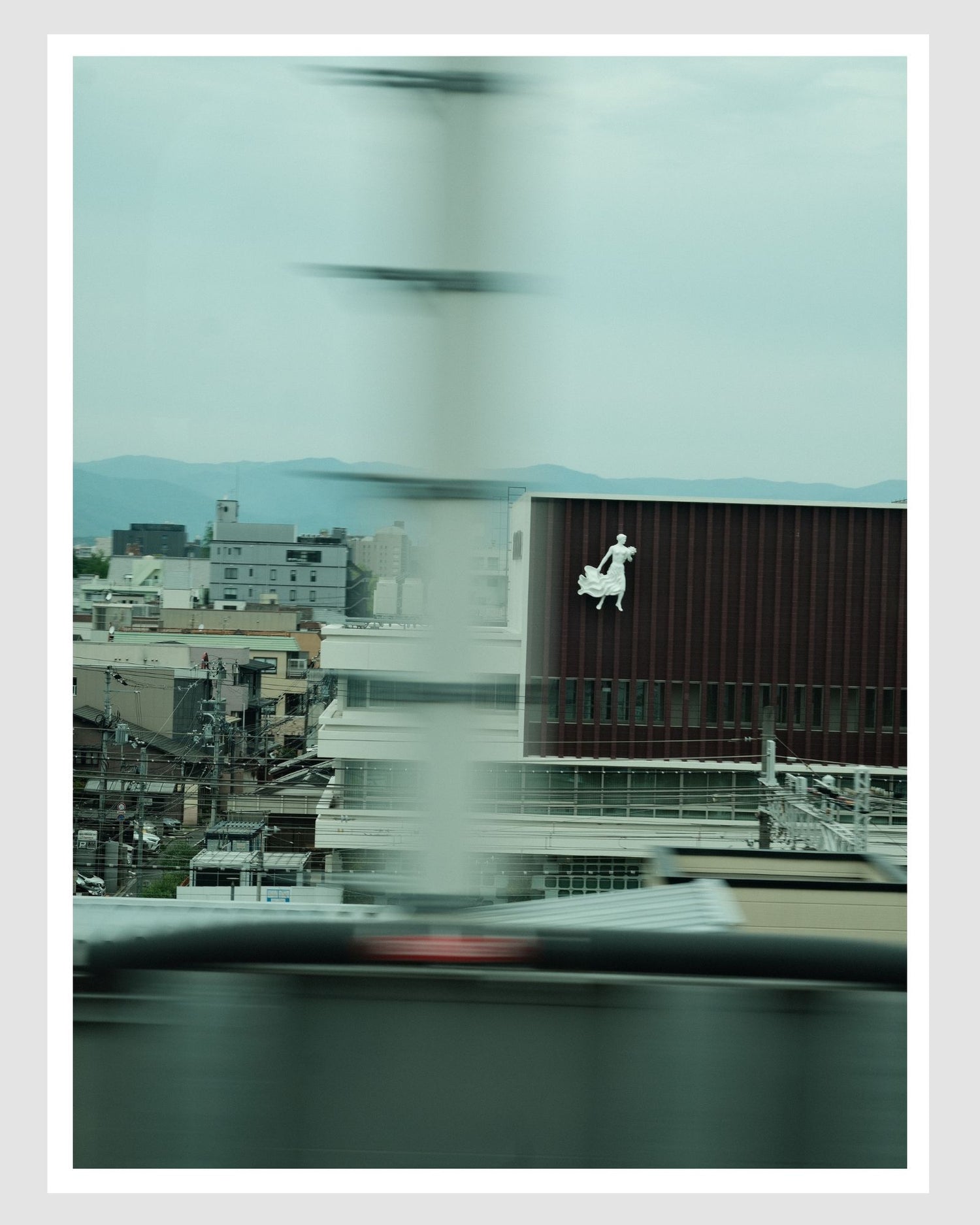 Cityscape view from a vehicle window with blurred motion, featuring a building with a logo.