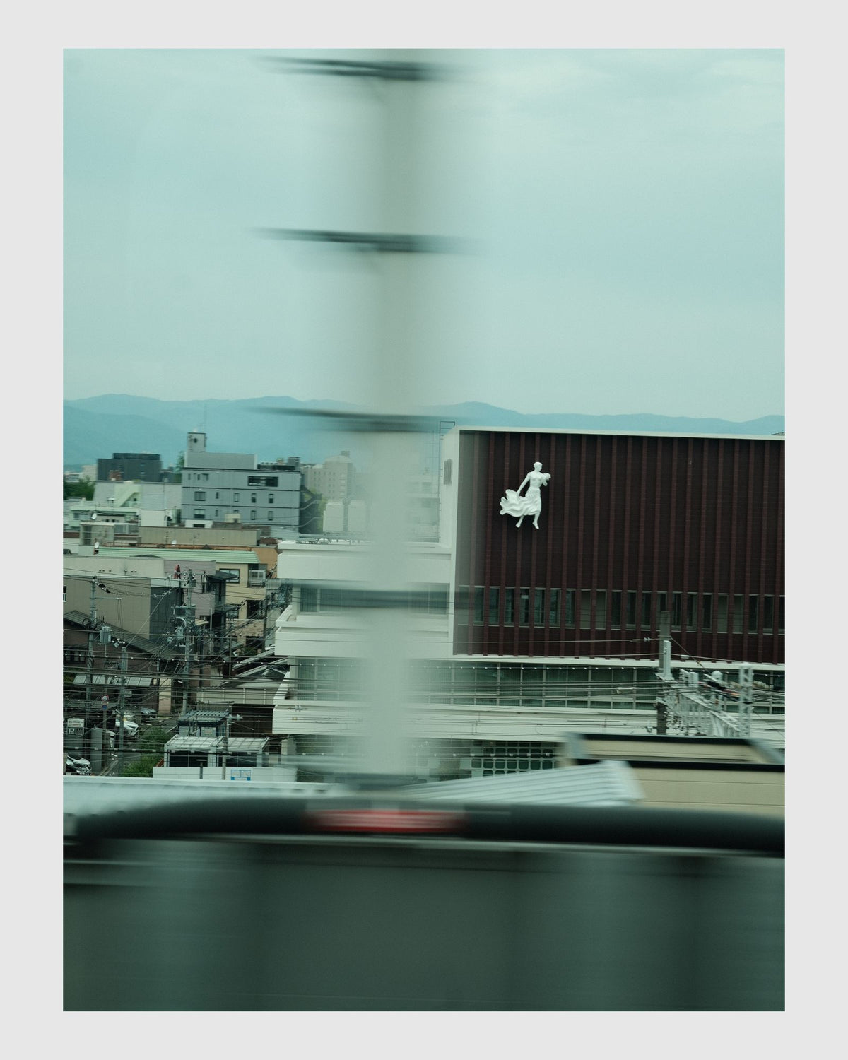 Cityscape view from a vehicle window with blurred motion, featuring a building with a logo.