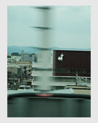 Cityscape view from a vehicle window with blurred motion, featuring a building with a logo.
