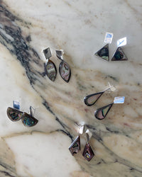 A group of silver and abalone earrings sit on a marble background from The Pared Store, Australia