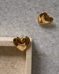 Gold heart earrings sit on a tray