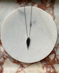 A sterling silver chain with a black carved angel wing sits on a marble plate