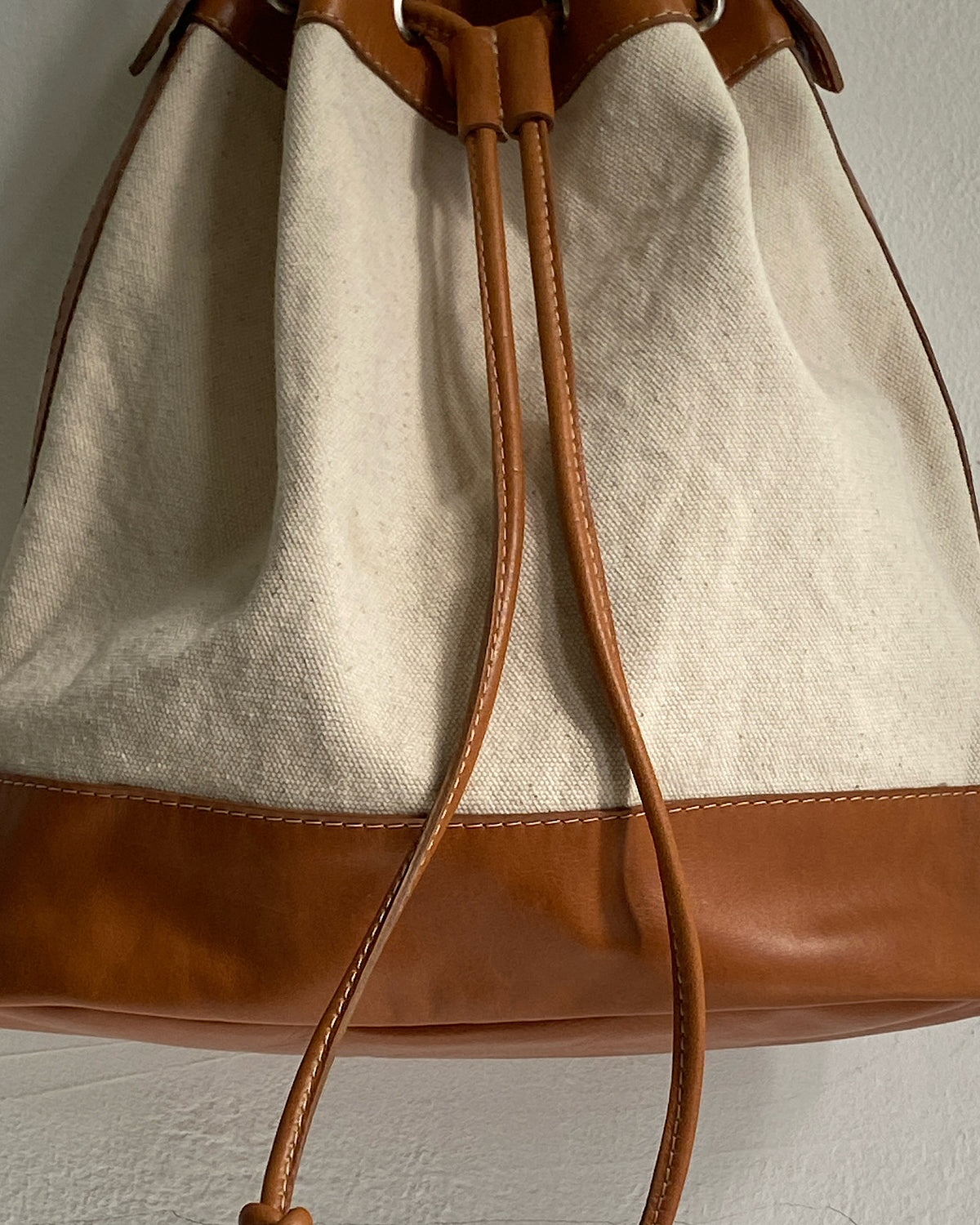 A tan trim canvas bucket bag sits on a wall The Pared Store