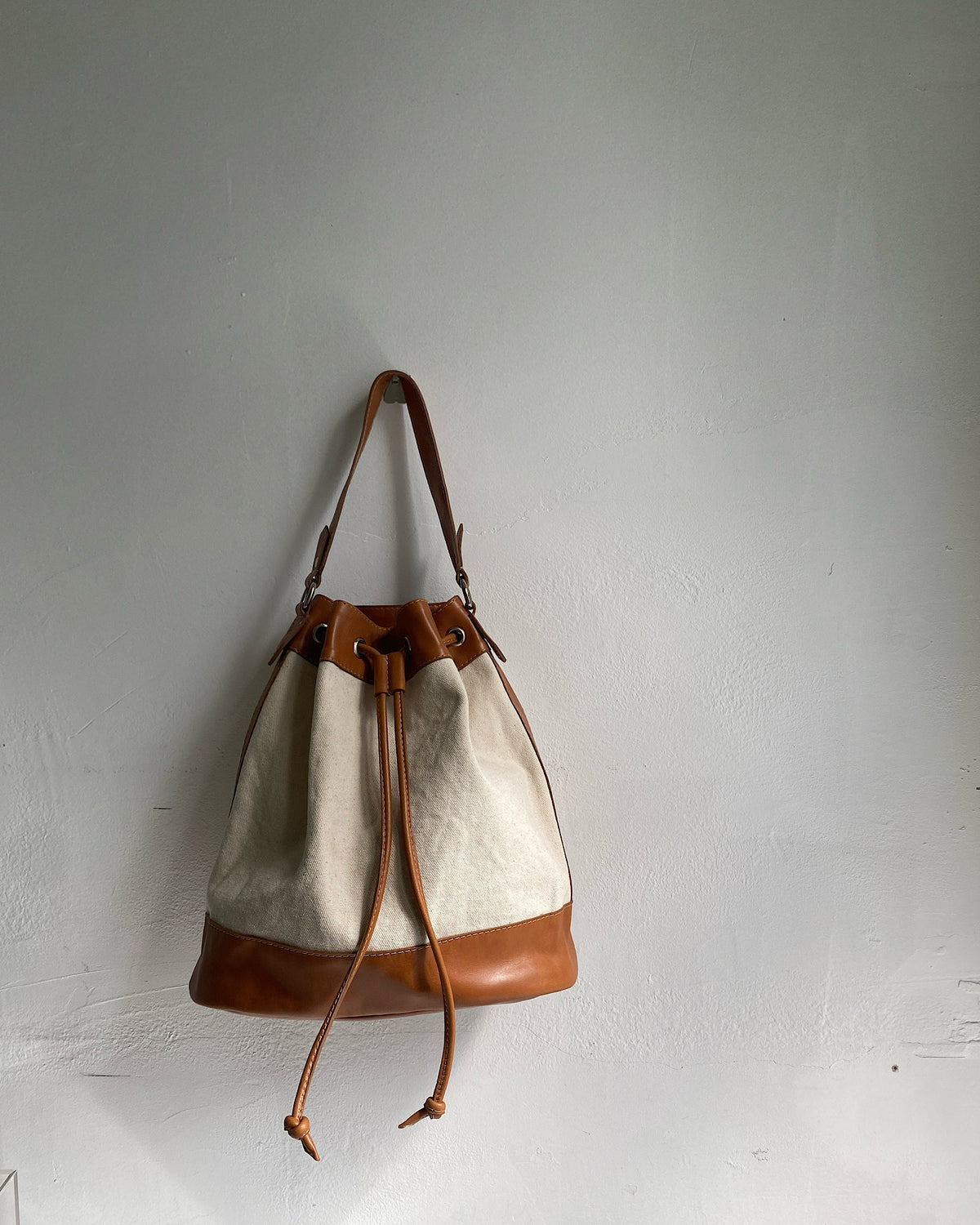 A tan trim canvas bucket bag sits on a wall The Pared Store