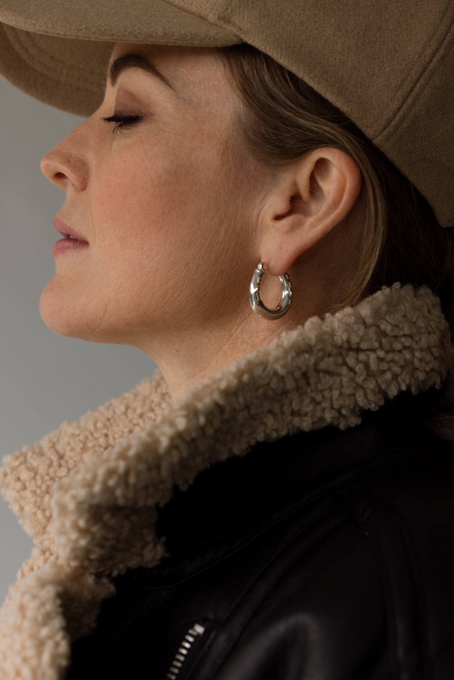 model wears horseshoe hoop earrings and a large jacket and cap