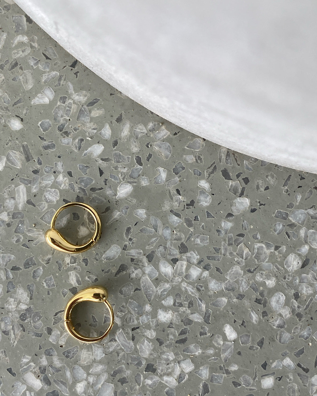 Small Gold organic Shaped Huggies sit on a terrazzo backdrop