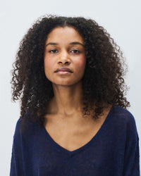 Woman with curly hair wearing a navy blue knit sweater from American Vintage against a light gray background
