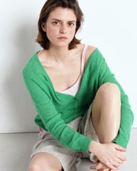 Woman wearing a green cardigan over a white top and grey shorts on a white background. Available at The Pared Store