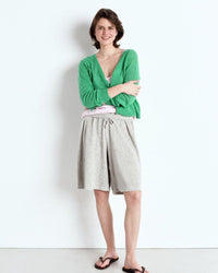 Woman wearing a green cardigan and grey shorts against a white background