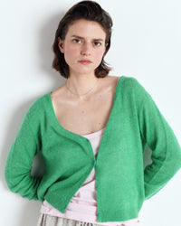 Woman wearing an American Vintage green cardigan over a pink top against a light background