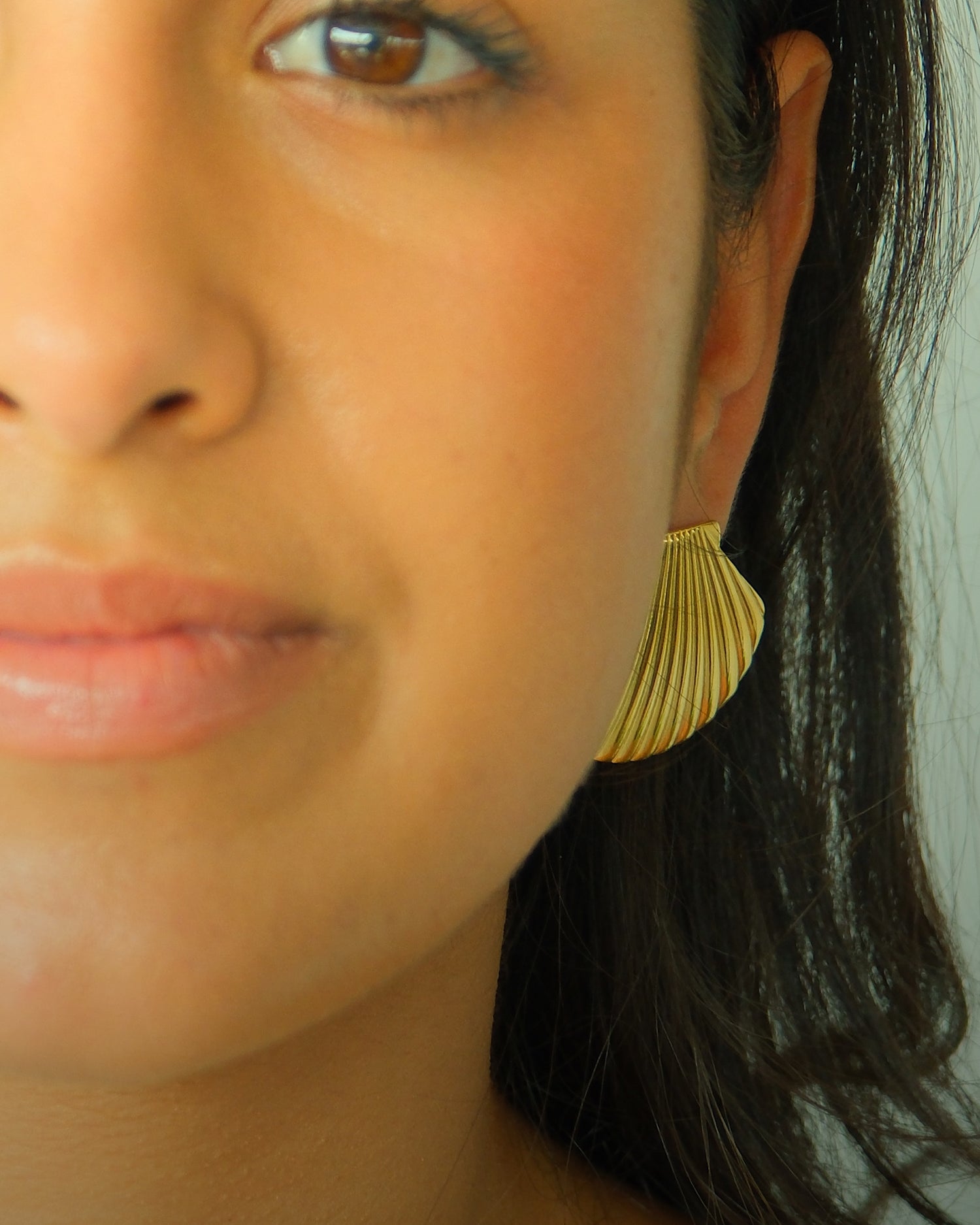 Model wears gold shell earrings from the Pared Store