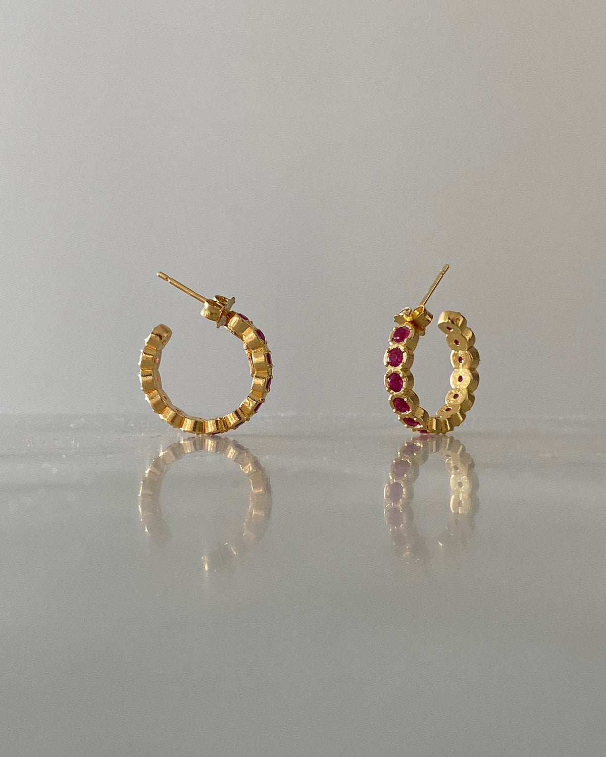 Gold hoop earrings inlaid with red crystals sit on a reflective surface