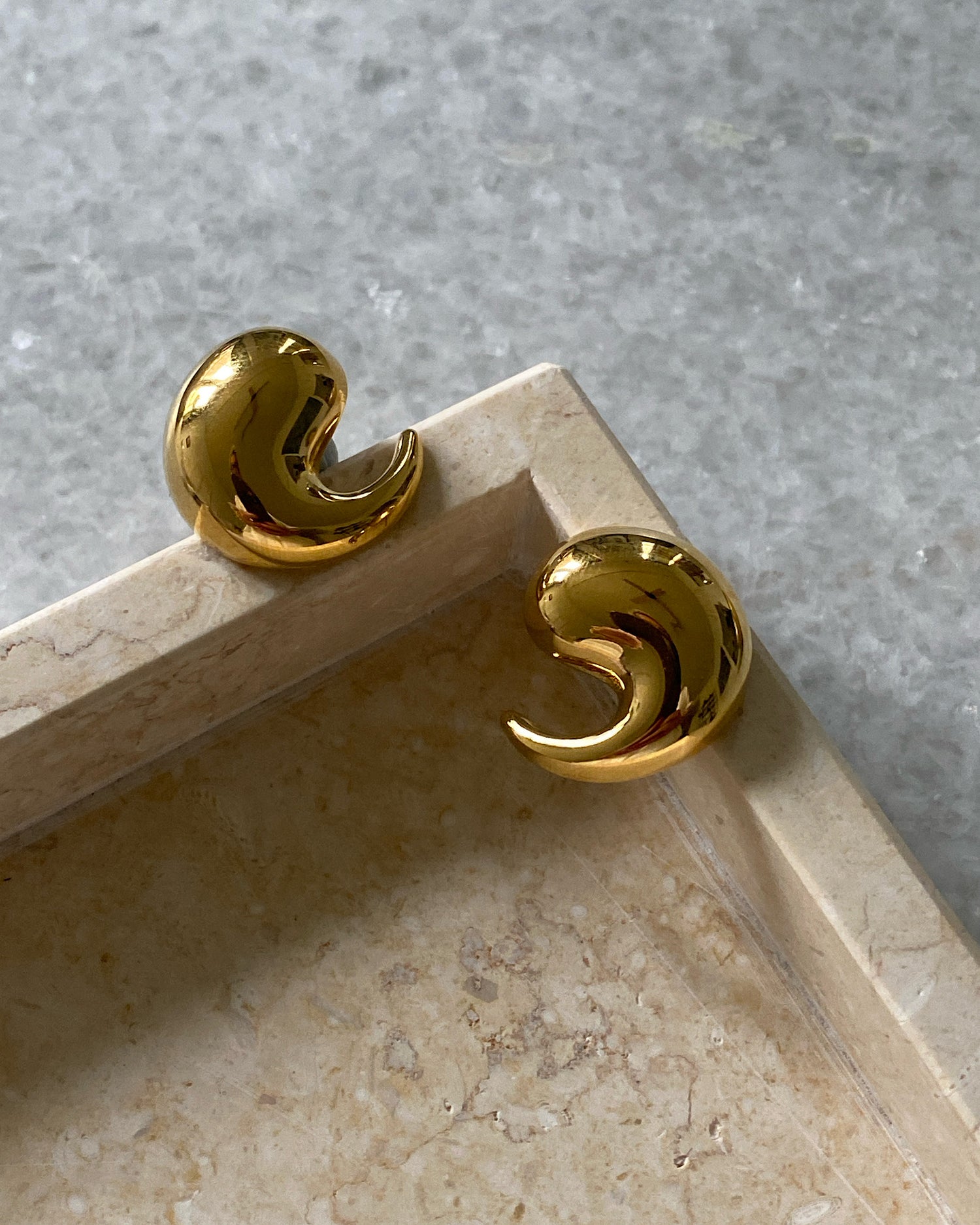 Gold swirl earrings on a tray