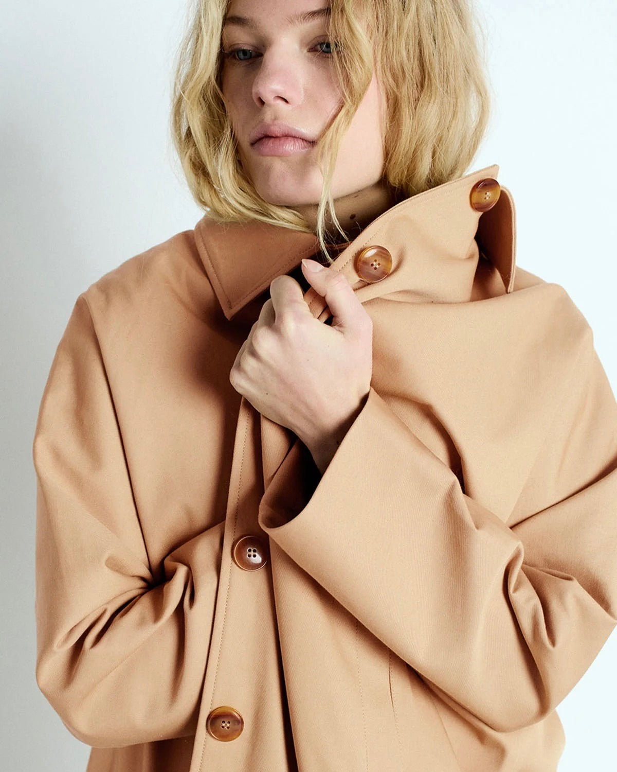 Woman wearing a beige coat with brown buttons on a white background