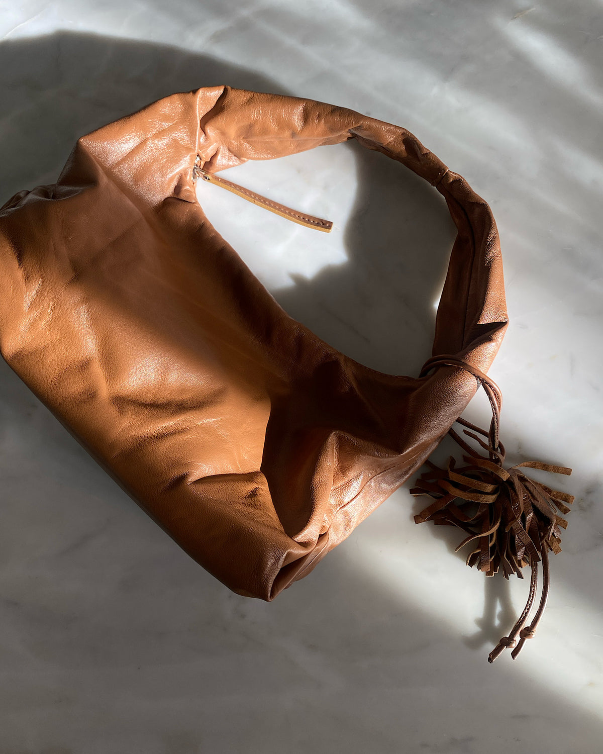 a tan shoulder bag lies on a marble top