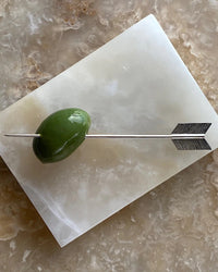 an olive sits on an arrow cocktail pick