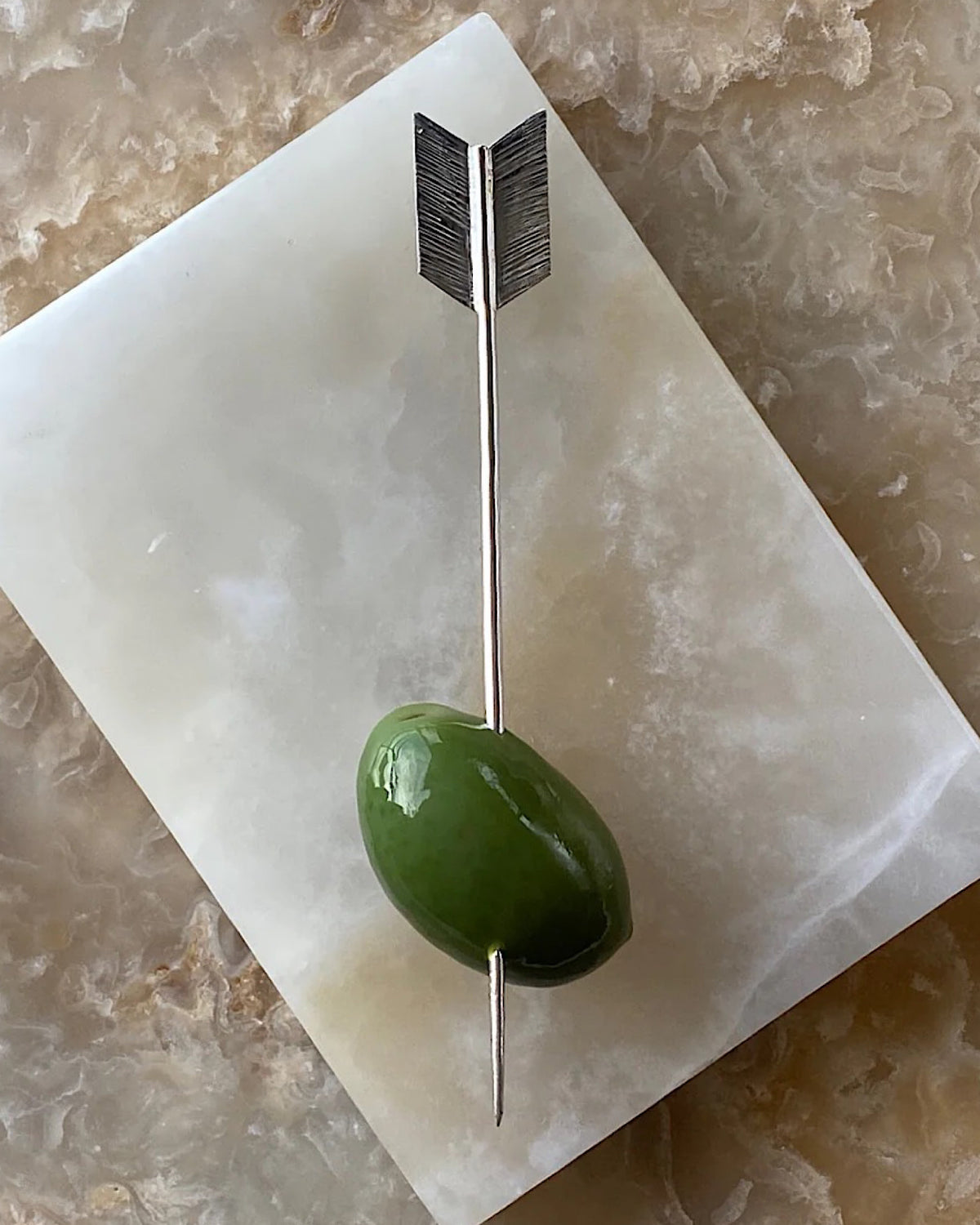 an olive sits on an arrow cocktail pick