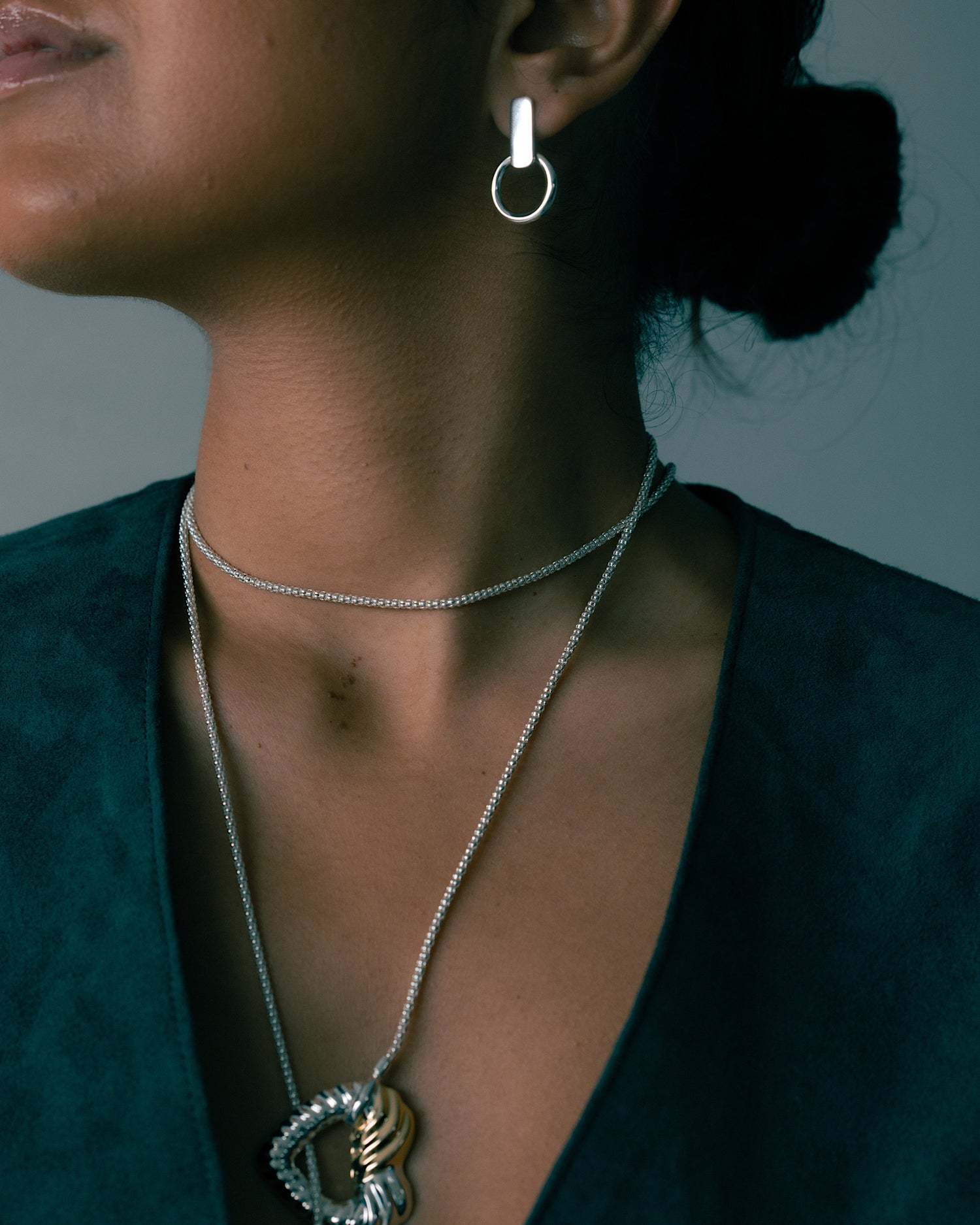 model wears a pair of silver earrings and a lariat chain on a suede vest