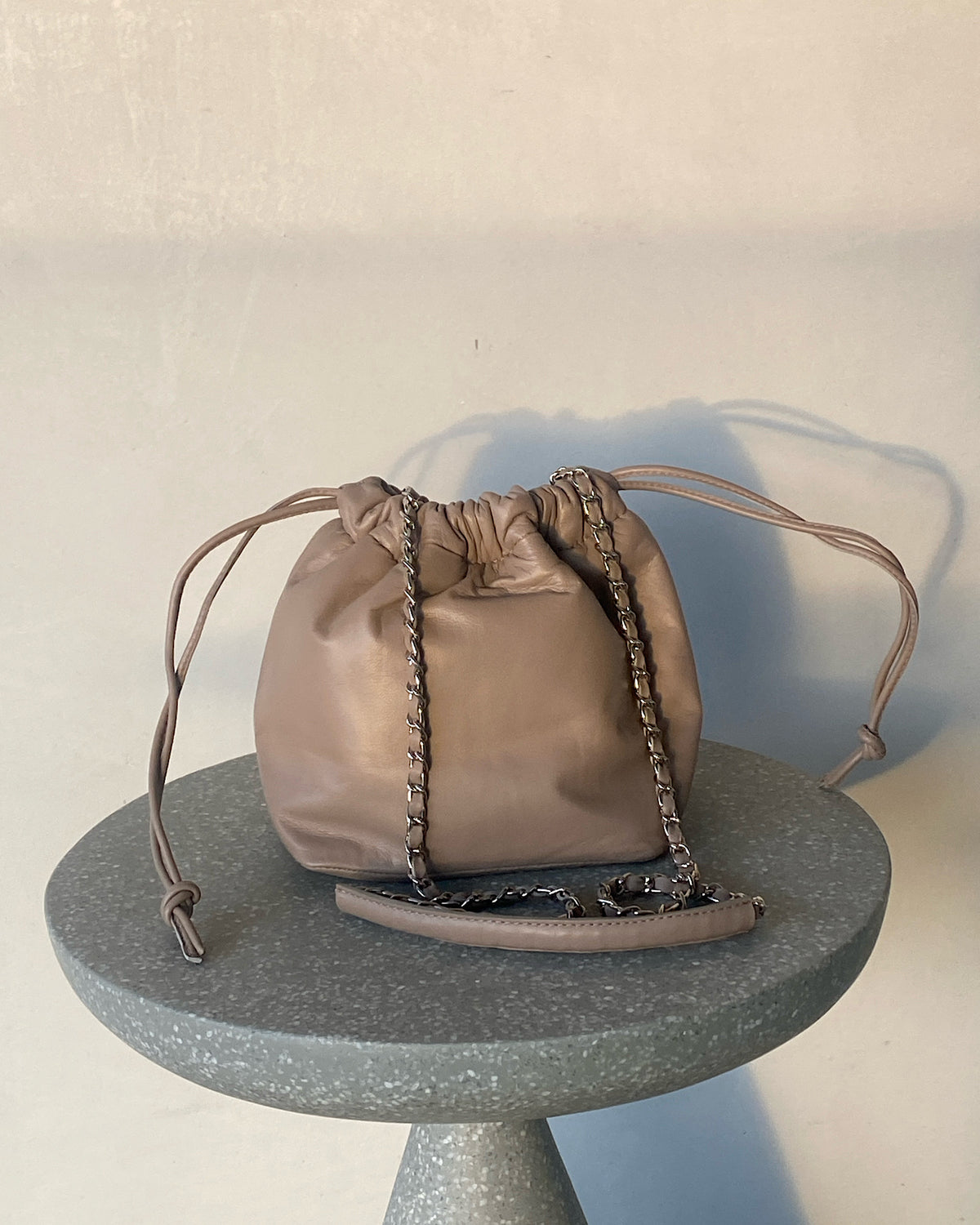 a taupe soft leather drawstring sits on a cement base