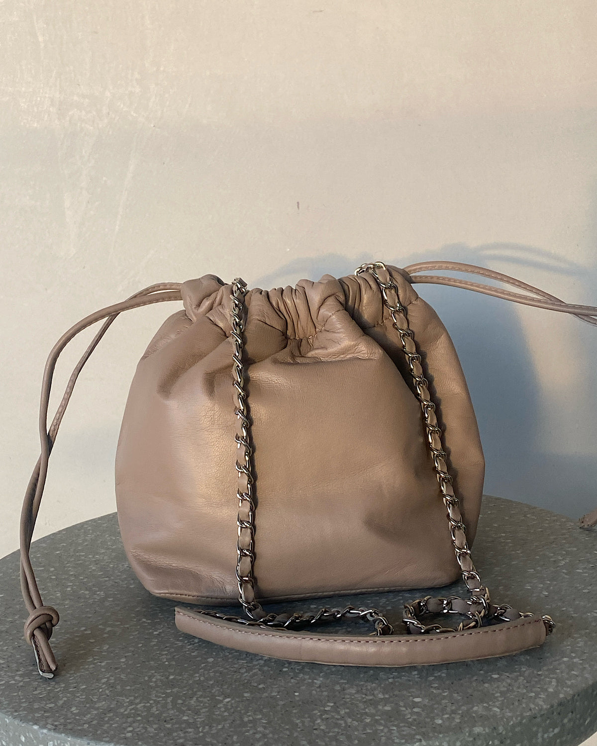 a taupe soft leather drawstring sits on a cement base