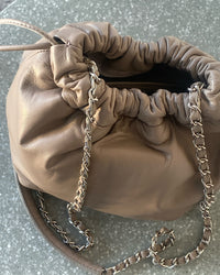 a taupe soft leather drawstring sits on a cement base